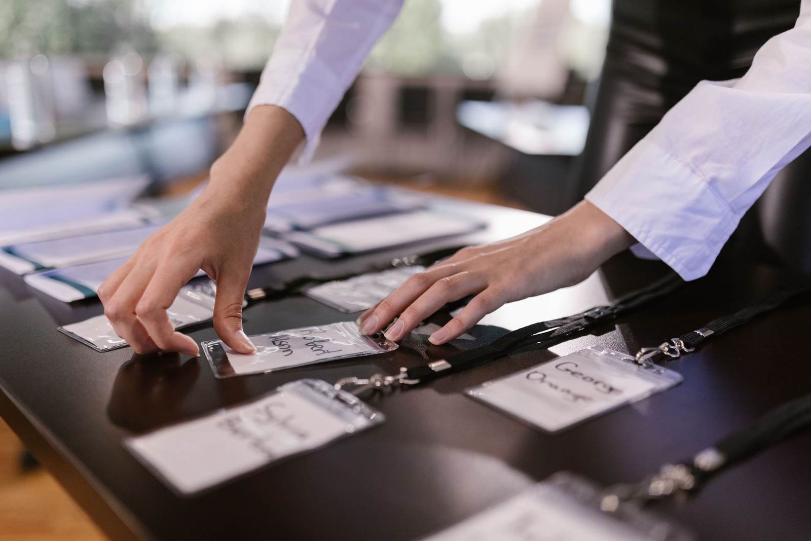 Two people’s hands arranging name badges and lanyards side by side on a dark conference registration table