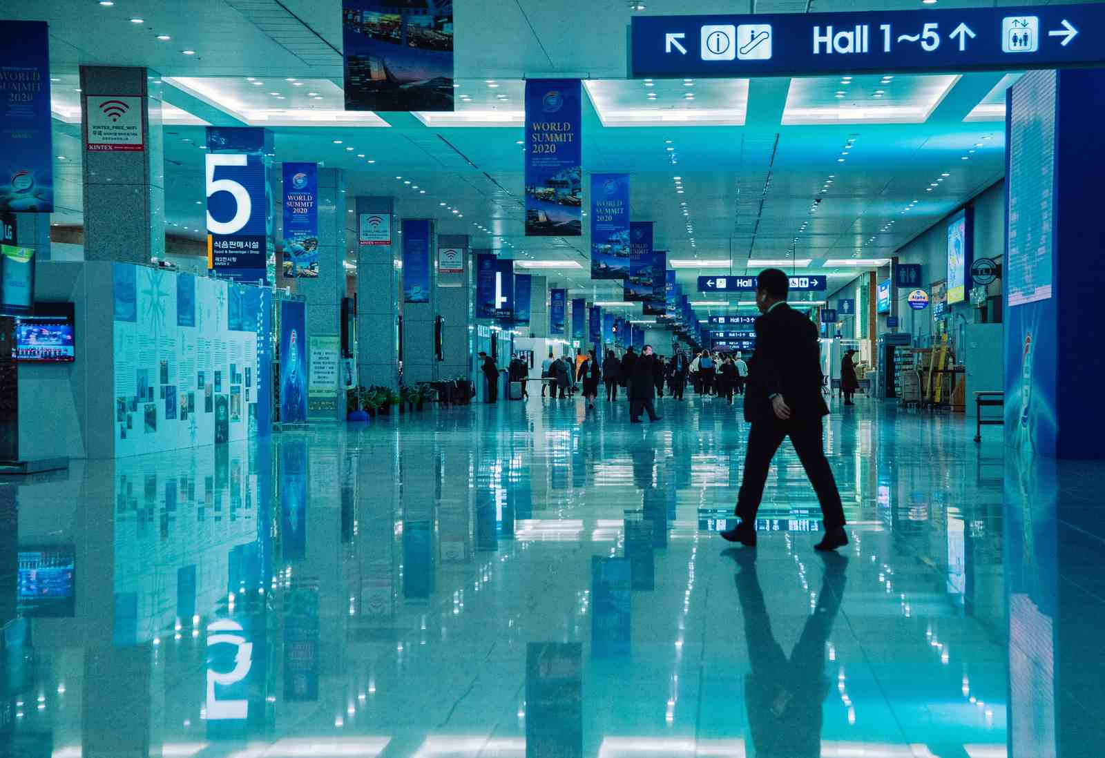 A delegate crosses the concourse of a convention centre beneath Hall 1-5 signage and summit banners