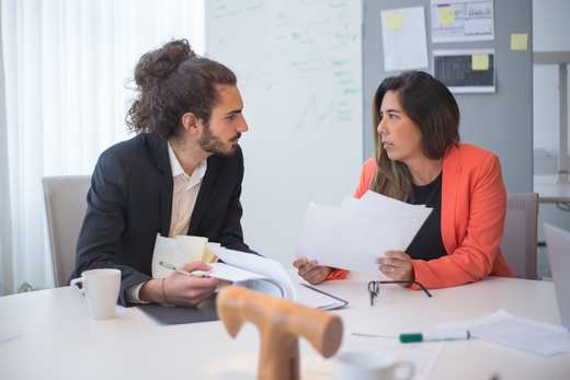 Two colleagues discuss a document across an office table