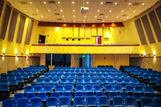 An empty auditorium with rows of blue upholstered seats, no people, facing a stage