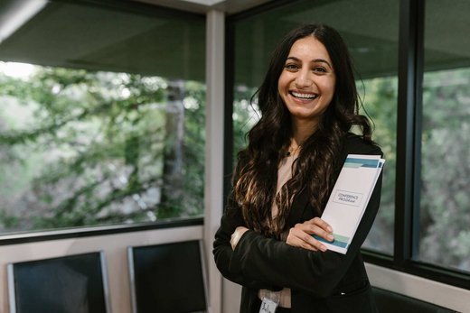 A smiling attendee holding a conference program in a bright lounge area between sessions