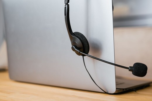 A headset microphone resting against the back of a laptop on a wooden desk