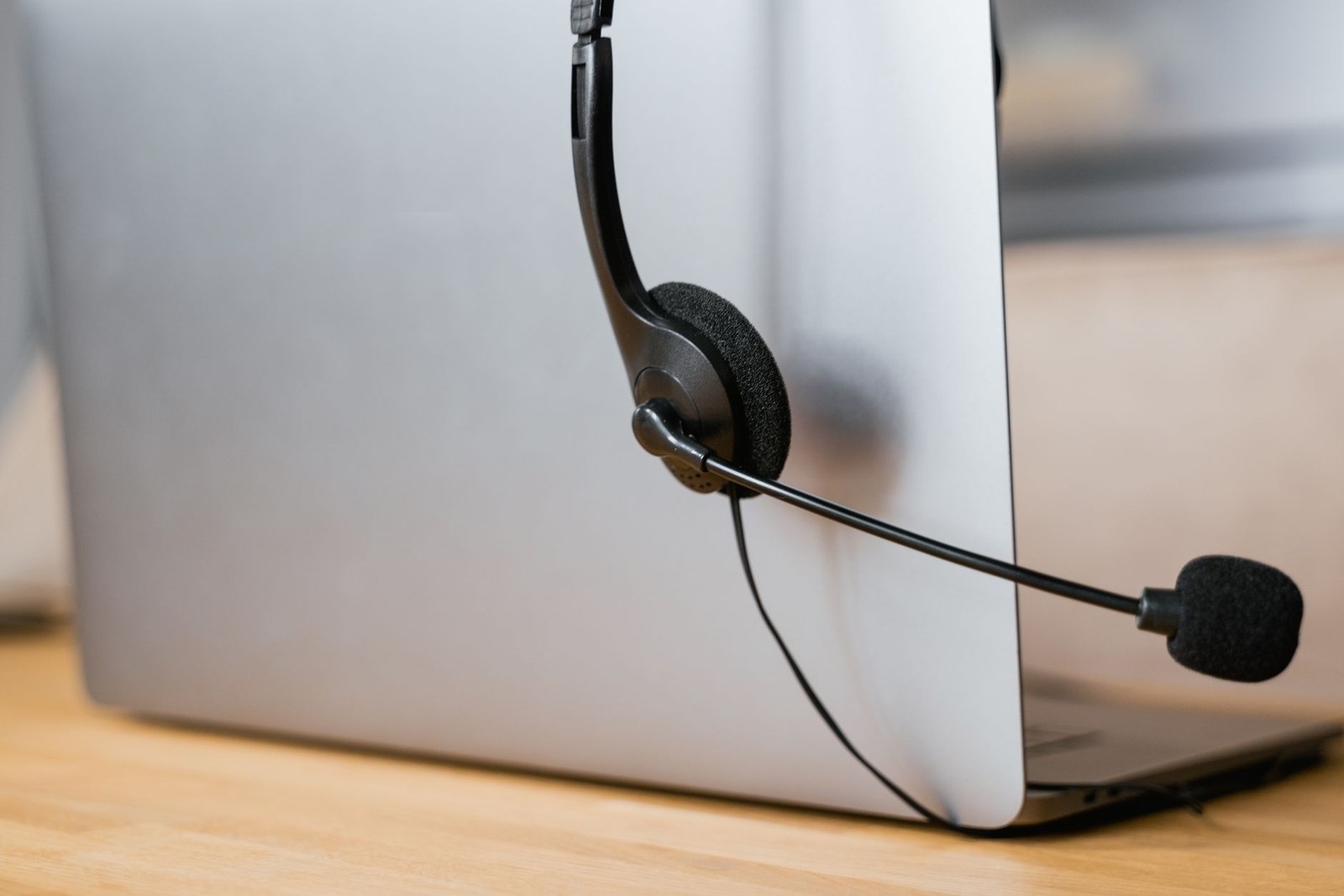 A headset microphone resting against the back of a laptop on a wooden desk