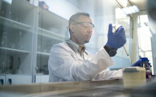 A scientist in safety glasses pipetting inside a biosafety cabinet