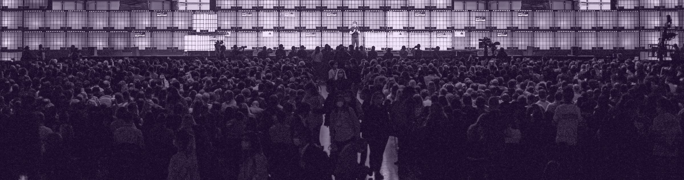An arena-scale conference crowd facing a glowing wall of panels