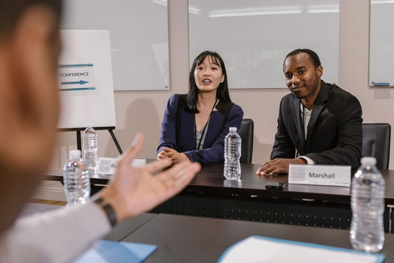 A panel discussion at a conference table, with a CONFERENCE-branded flip chart visible in the background