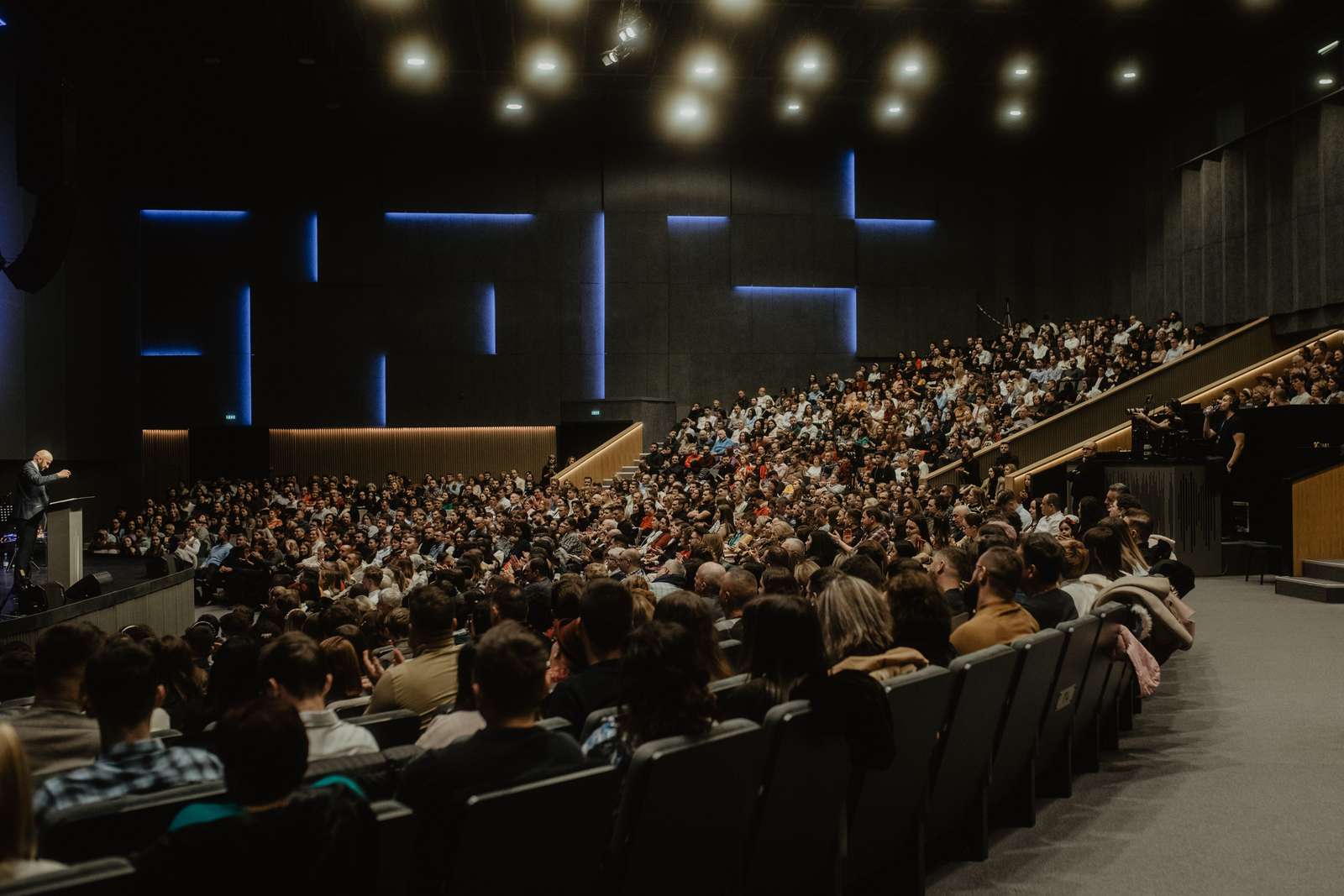 A full auditorium listening to a speaker at a lectern during a conference plenary