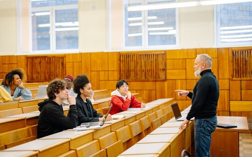 An instructor addressing students seated in tiered lecture-hall rows during a training session