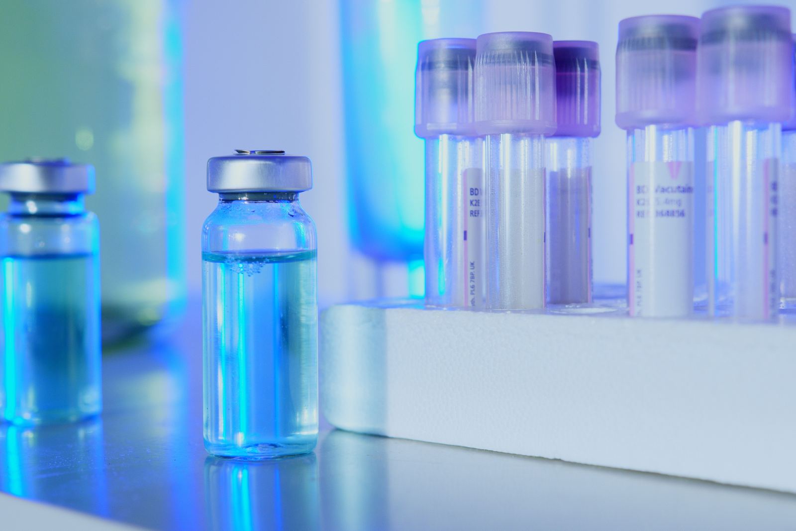 Glass vials and racked sample tubes on a bench in a blue-lit testing laboratory
