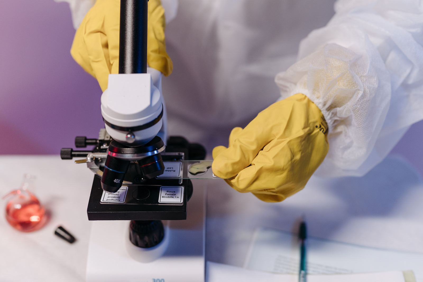A researcher in protective gloves and gown placing a sample slide under a microscope