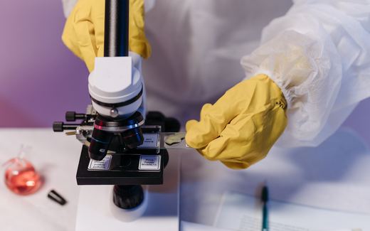 A gloved researcher placing a sample slide under a microscope