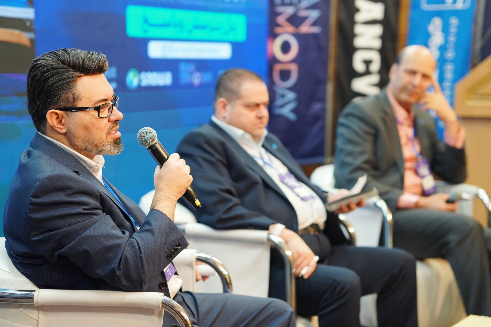 Four panelists in business attire seated on stage during a legal and regulatory conference panel discussion, one speaking into a microphone