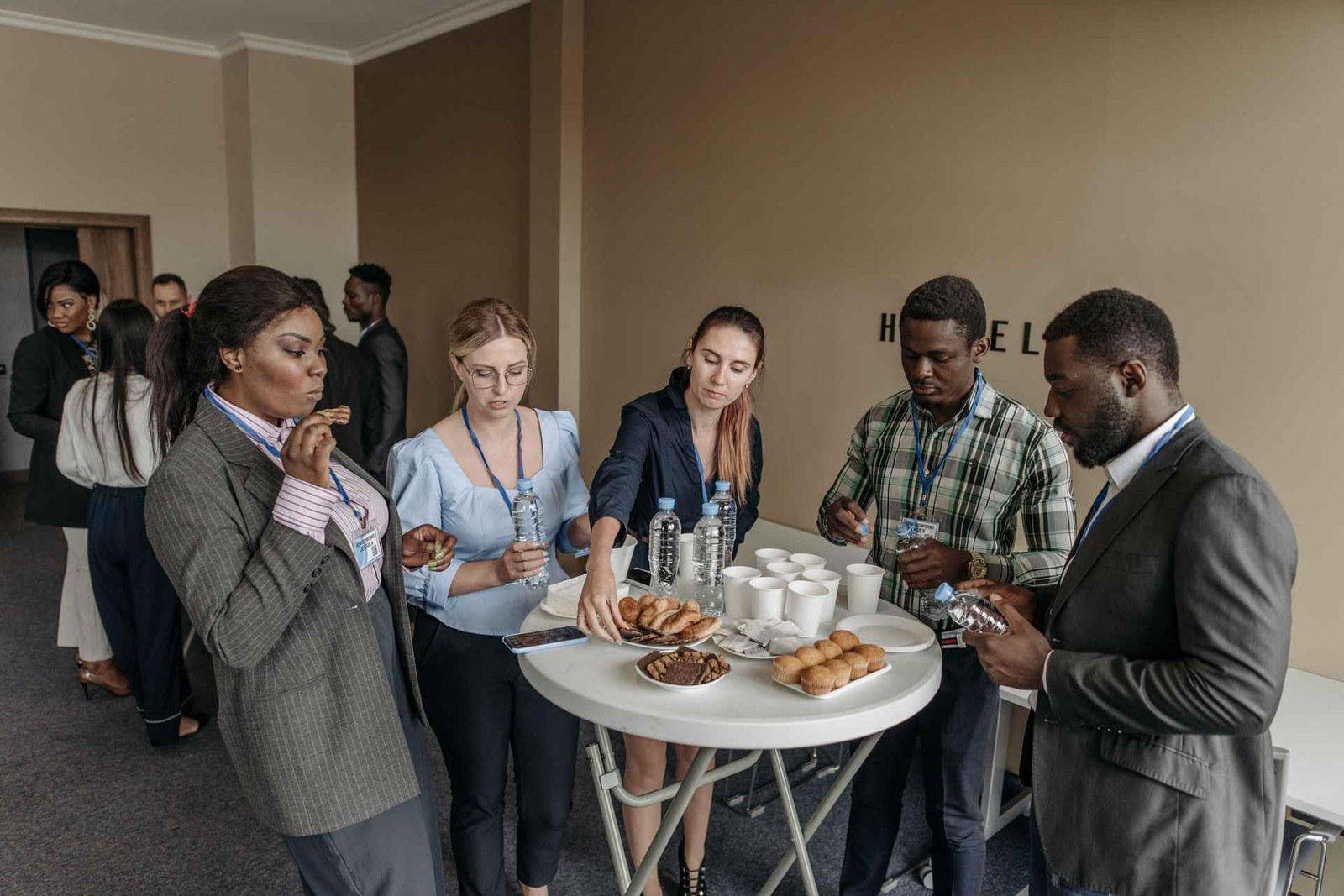 Conference attendees wearing lanyards gather around a table of refreshments during a break