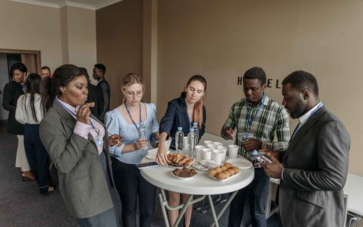 Conference attendees wearing lanyards gather around a table of refreshments during a break