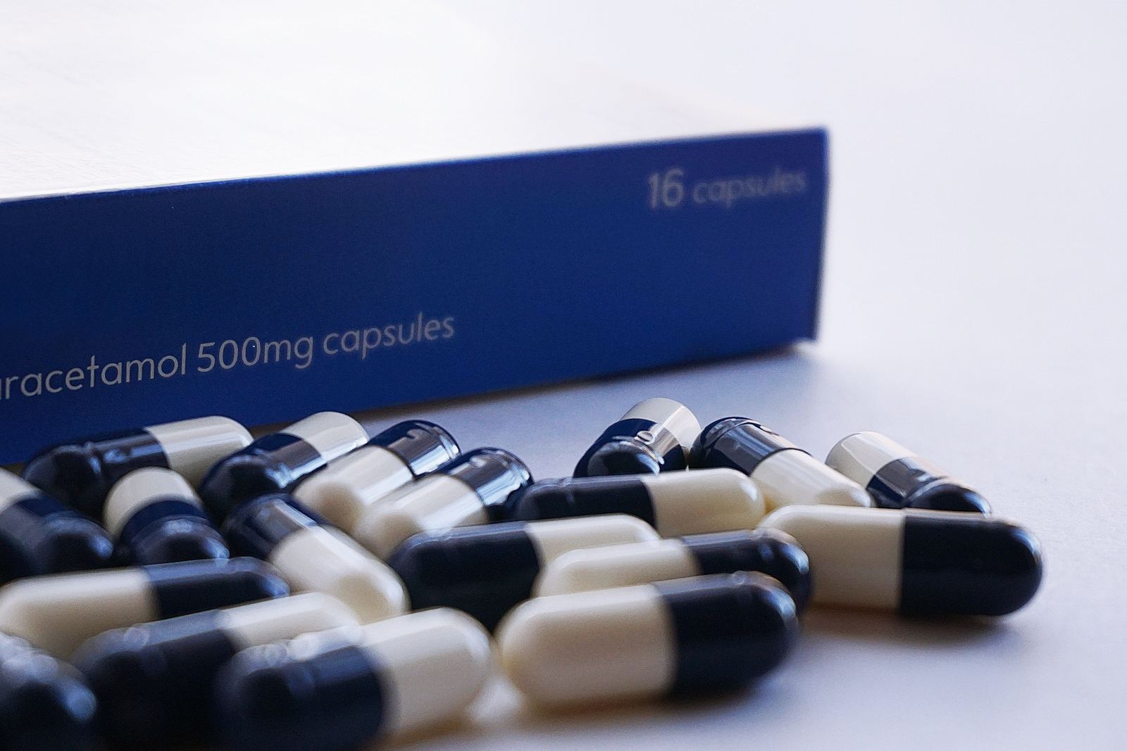 A blue box of paracetamol 500mg capsules with loose blue-and-white capsules in front of it