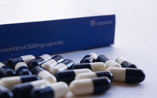 A blue box of paracetamol capsules with loose capsules in front of it