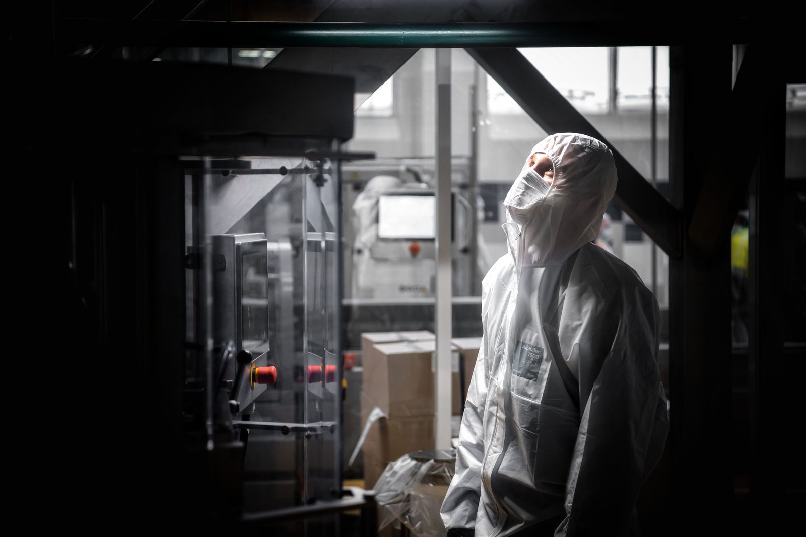 A worker in white sterile coveralls and mask standing beside equipment on a pharmaceutical production line
