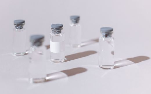 Clear glass injection vials with grey stoppers on a white surface
