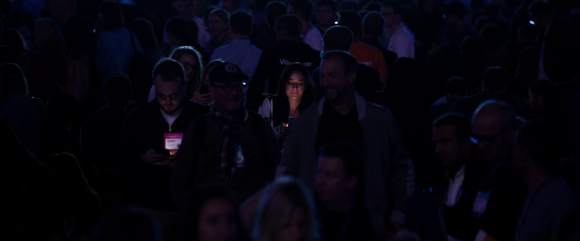 A conference crowd at night, faces lit by the room's glow