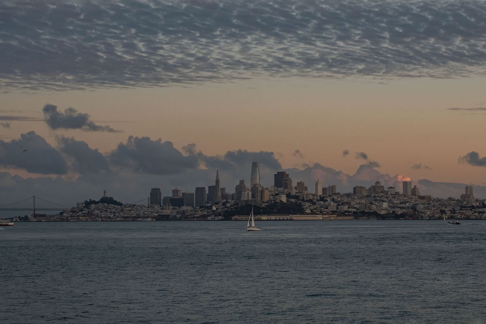 The San Francisco skyline at sunset seen across the bay, with a sailboat in the foreground