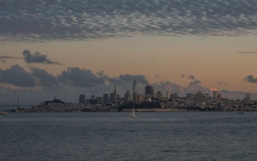 The San Francisco skyline at sunset seen across the bay, with a sailboat in the foreground
