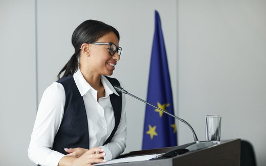 A regulatory professional speaking from a lectern with the EU flag behind her