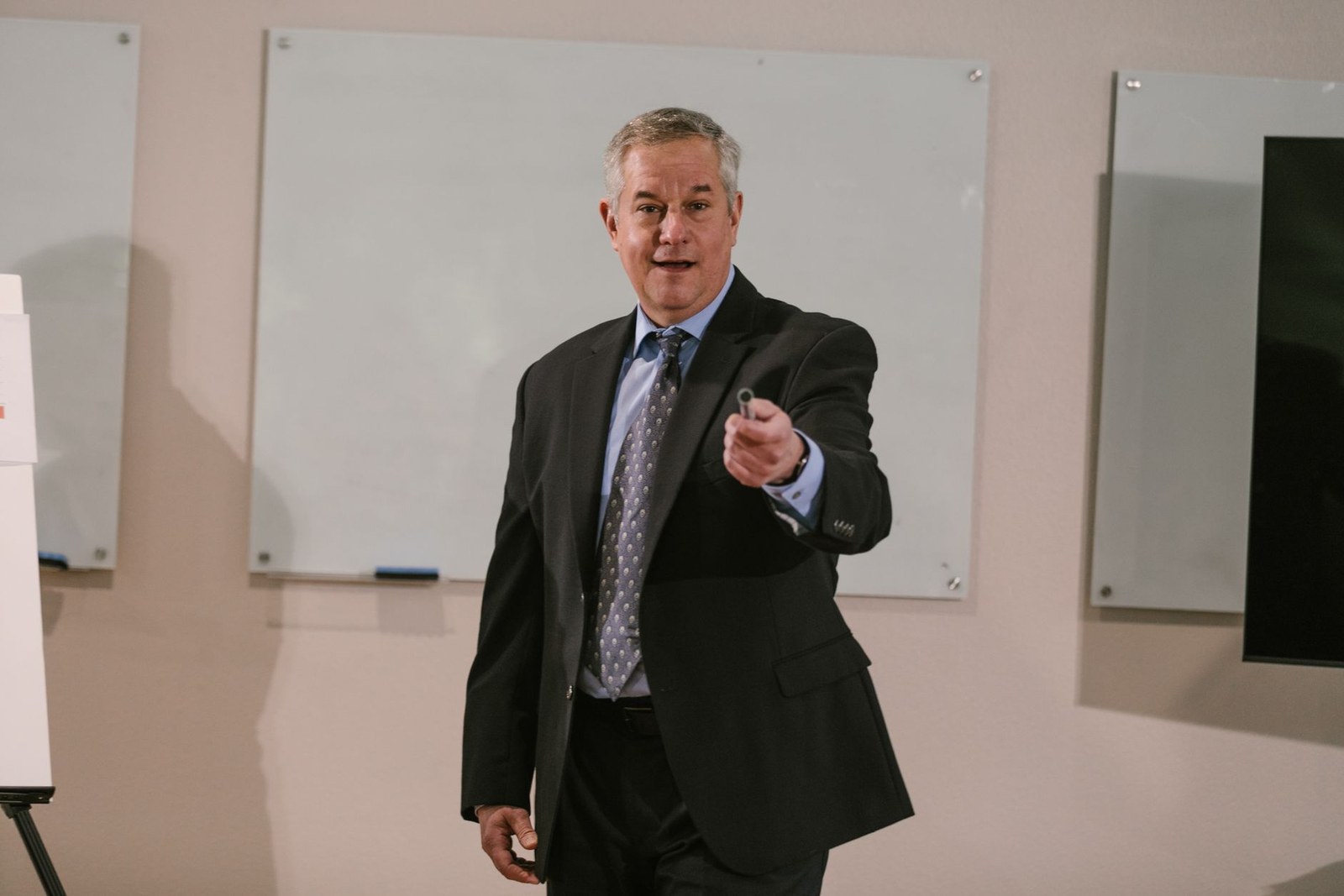 A presenter in a suit gestures while speaking to a small group in a training room