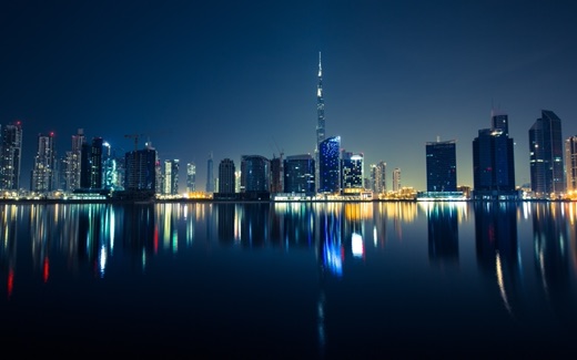 The Dubai skyline at night with the Burj Khalifa reflected in still water